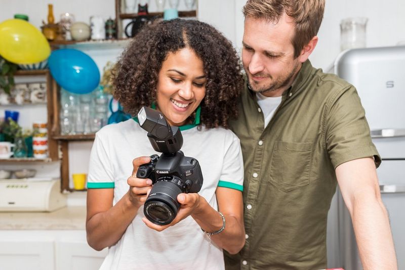 Een vrouw en een man lachen terwijl ze naar het scherm van een Canon-camera met een bevestigde Canon Speedlite EL-100 kijken.