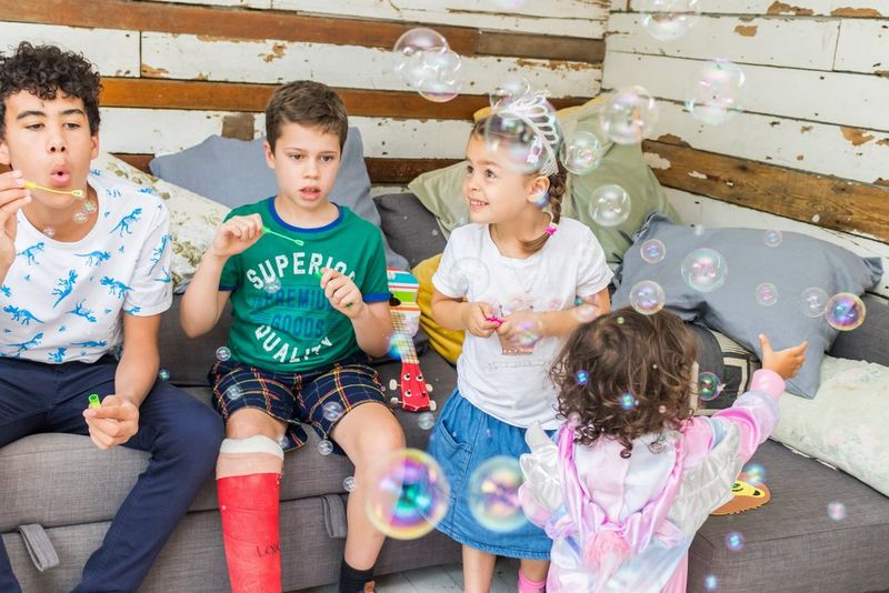 Twee kinderen gebruiken bellenblazers terwijl twee andere kinderen toekijken en met de bellen spelen. Gefotografeerd met een Canon Speedlite EL-100-flitser.
