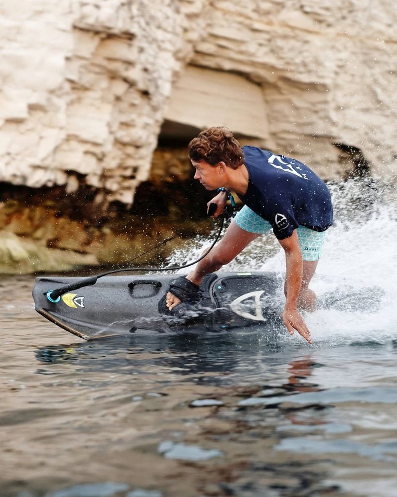 Surfista che si inclina sul lato di un jetboard, in posizione quasi parallela rispetto all'acqua. La sua mano è appena sopra la superficie.