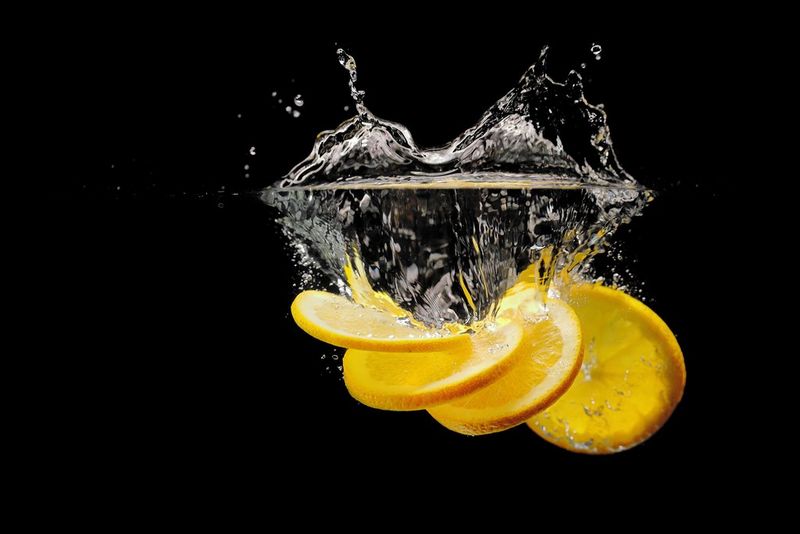 Fette di limone che cadono nell'acqua immobile, su uno sfondo totalmente nero.