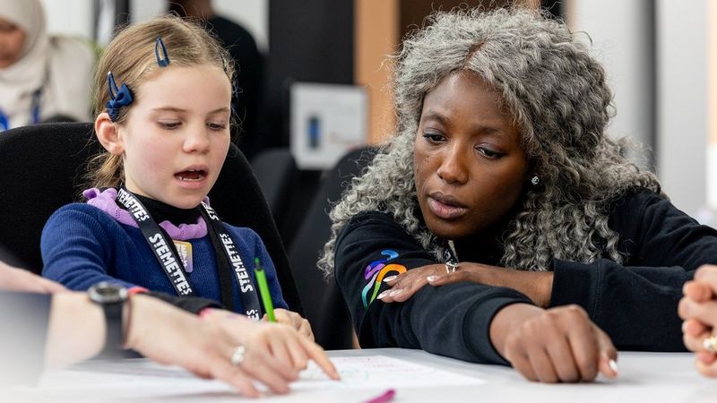 Dr Anne-Marie Imafidon MBE helps a young Stemette as she writes down her ideas.