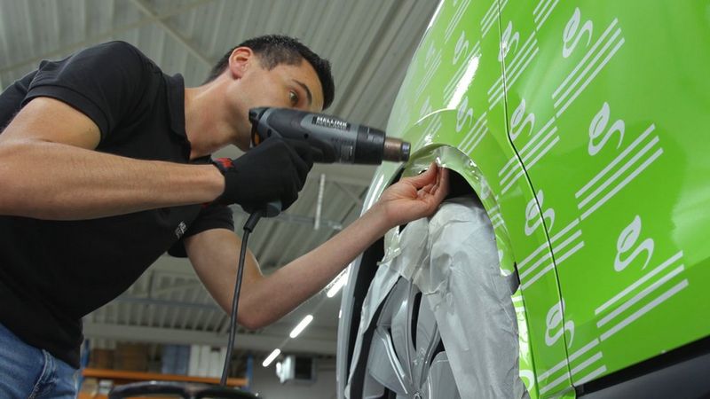 Ein Techniker bringt mit einem Heißluftgebläse vorsichtig eine leuchtend grüne Vinylfolie um den Radkasten eines Fahrzeugs an.