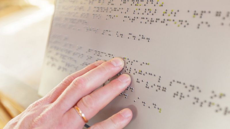 Eine Hand berührt ein in der Blindenschrift Braille geschriebenes Zeichen.
