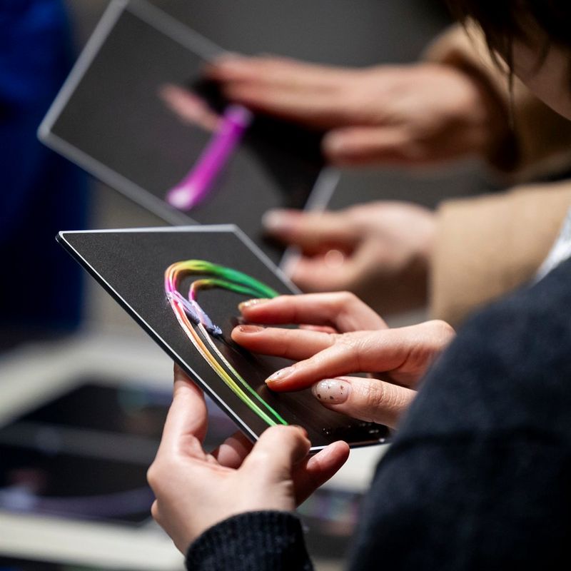 Two pairs of small hands hold and run their fingers over tactile photographs.