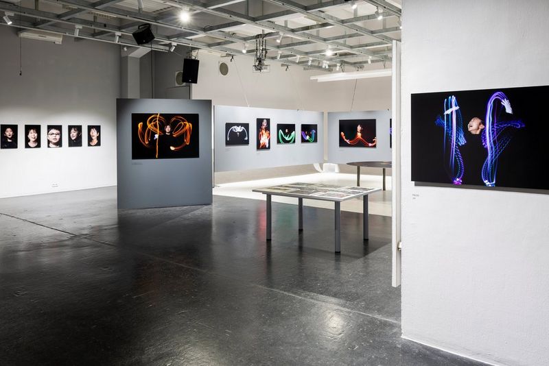 A photo gallery with accent lighting mounted on a grid on the ceiling and pictures displayed on off-white walls.