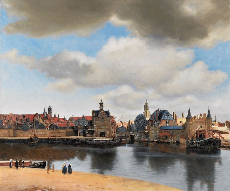 View of Delft by Johannes Vermeer. A cloudy sky over the river Schie, with the Schiedam Gate in the middle of the composition, and the Rotterdam Gate and its barbican to the right, all reflected in the water of the harbour.