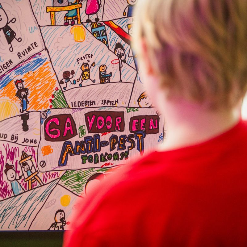 The head and shoulders of a young person from behind. The are looking at a hand drawn anti-bullying poster.