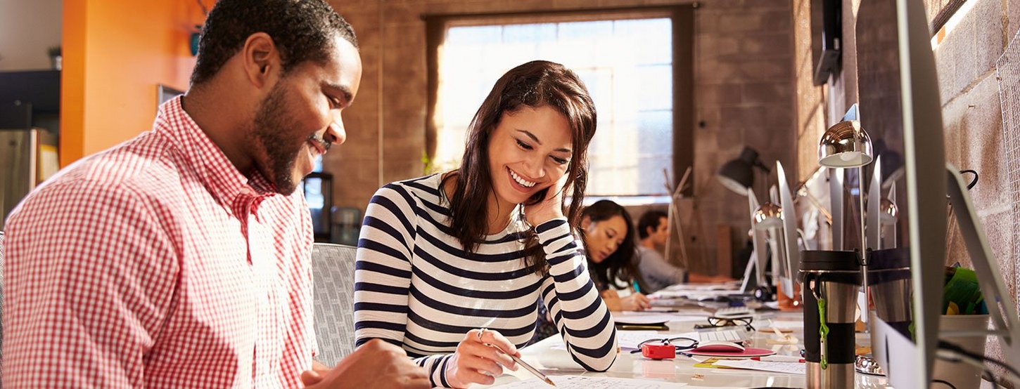 Man and woman sat smiling and chatting over work at desk in a creative studio