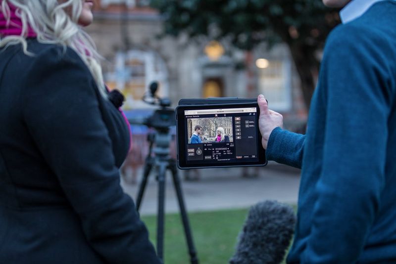 A user holds a tablet running Canon's Browser Remote app, showing a preview of the image from a Canon camcorder pointing at them.
