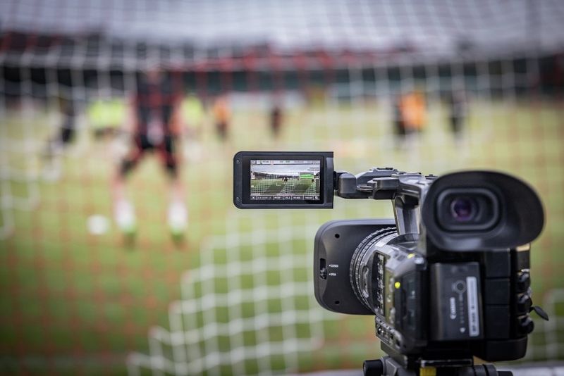 A Canon XF605 camcorder positioned behind the goal during a football game, filming through the net.