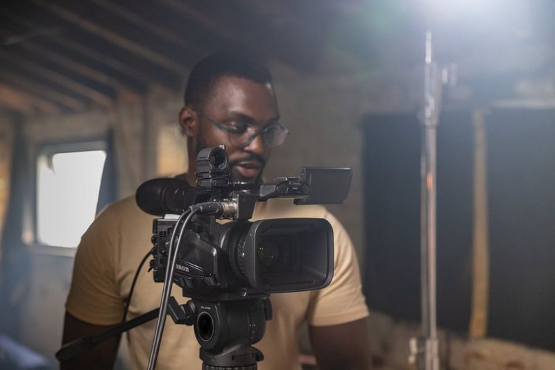 A man shooting indoors with a Canon XF605 on a tripod. 
