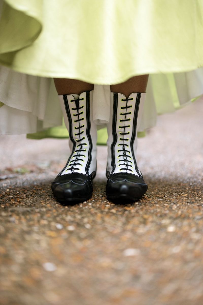 A close-up of feet peeking out of the bottom of a dress. The dress is a lime green, and the boots have black and white vertical stripes.