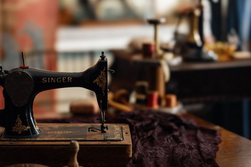 An old-fashioned sewing machine sits on a desk. Dark purple fabric is positioned under the machine.