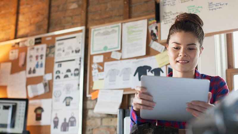 Young woman smiling at tablet in exposed brick office with mood boards on wall behind her