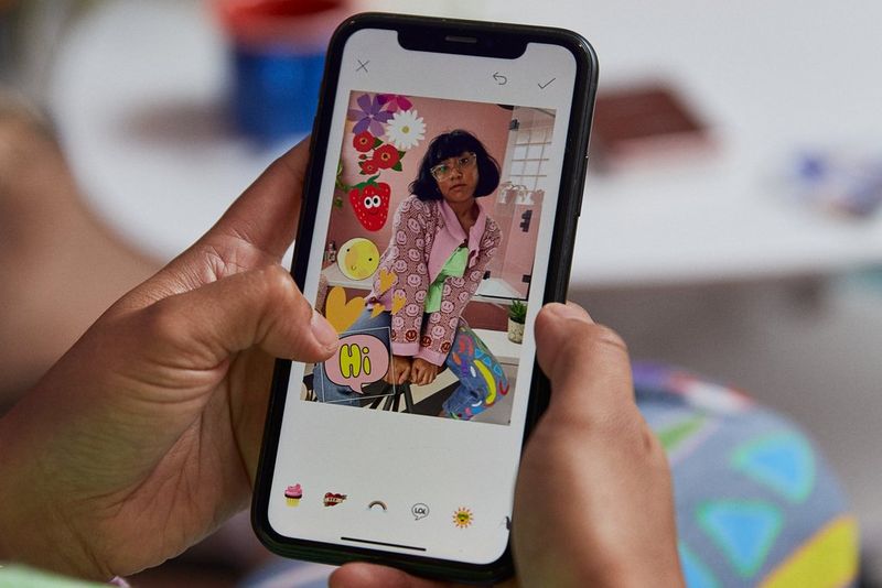 Ruke drže telefon prilikom dodavanja naljepnica slici u aplikaciji Canon Mini PRINT.