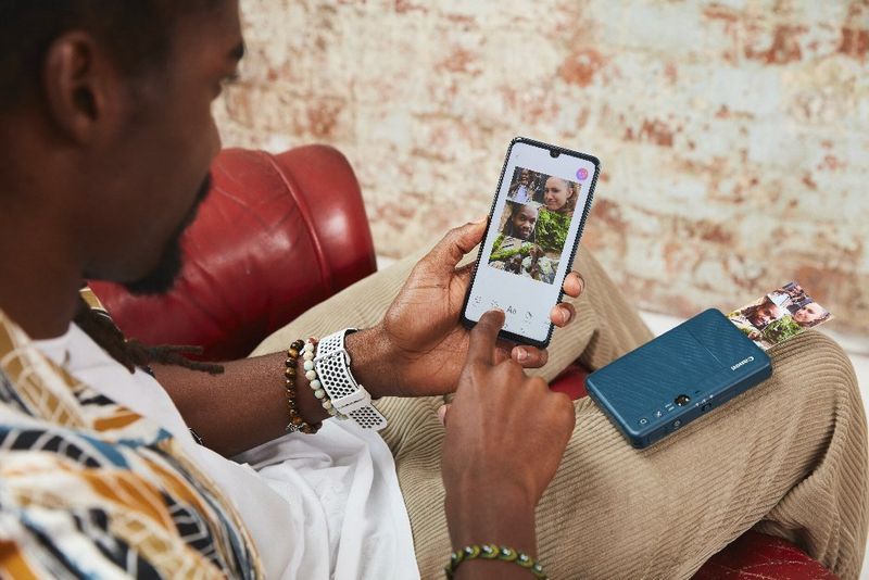 Un jeune homme aux cheveux longs assis sur une chaise utilise son téléphone portable pour imprimer une image sur le Canon Zoemini S2.