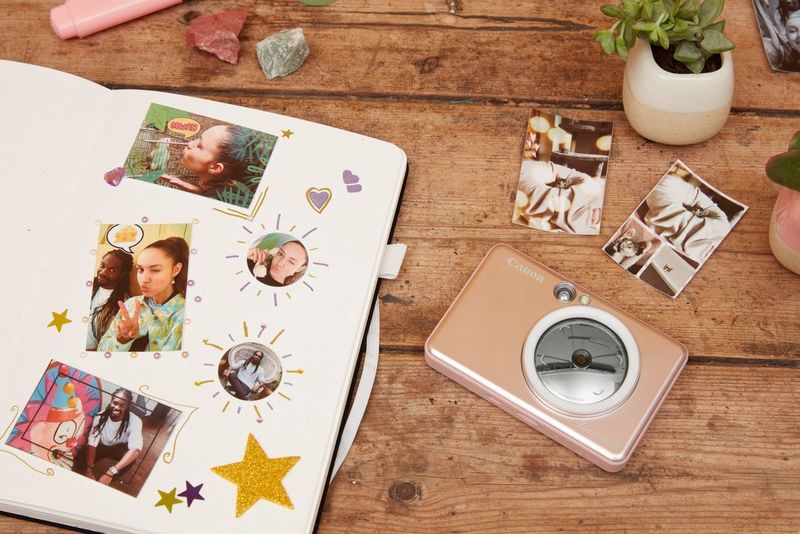 Un Canon Zoemini S2 et un album sur un bureau montrant des photos d'un jeune homme et de femmes qui font des grimaces et s'amusent.