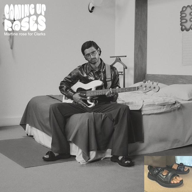 Imagen en blanco y negro de un hombre sentado en el borde de una cama sosteniendo una guitarra