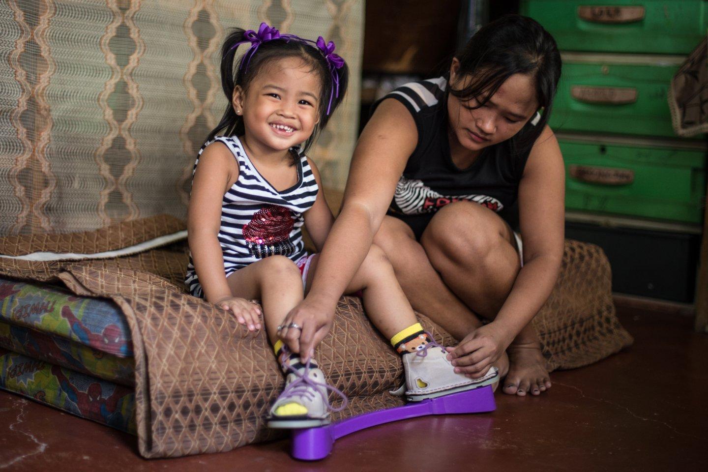 A baby in a plaster cast receiving treatment from MiracleFeet and a young child sat smiling also recieving treatment.