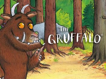 The Gruffalo stood amongst some trees pointing to the Gruffalo logo