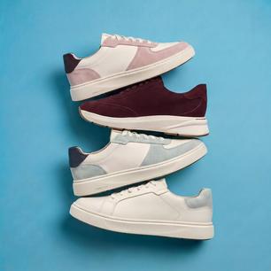 Clarks trainers in pink, burgundy, grey and white arranged against a blue background.