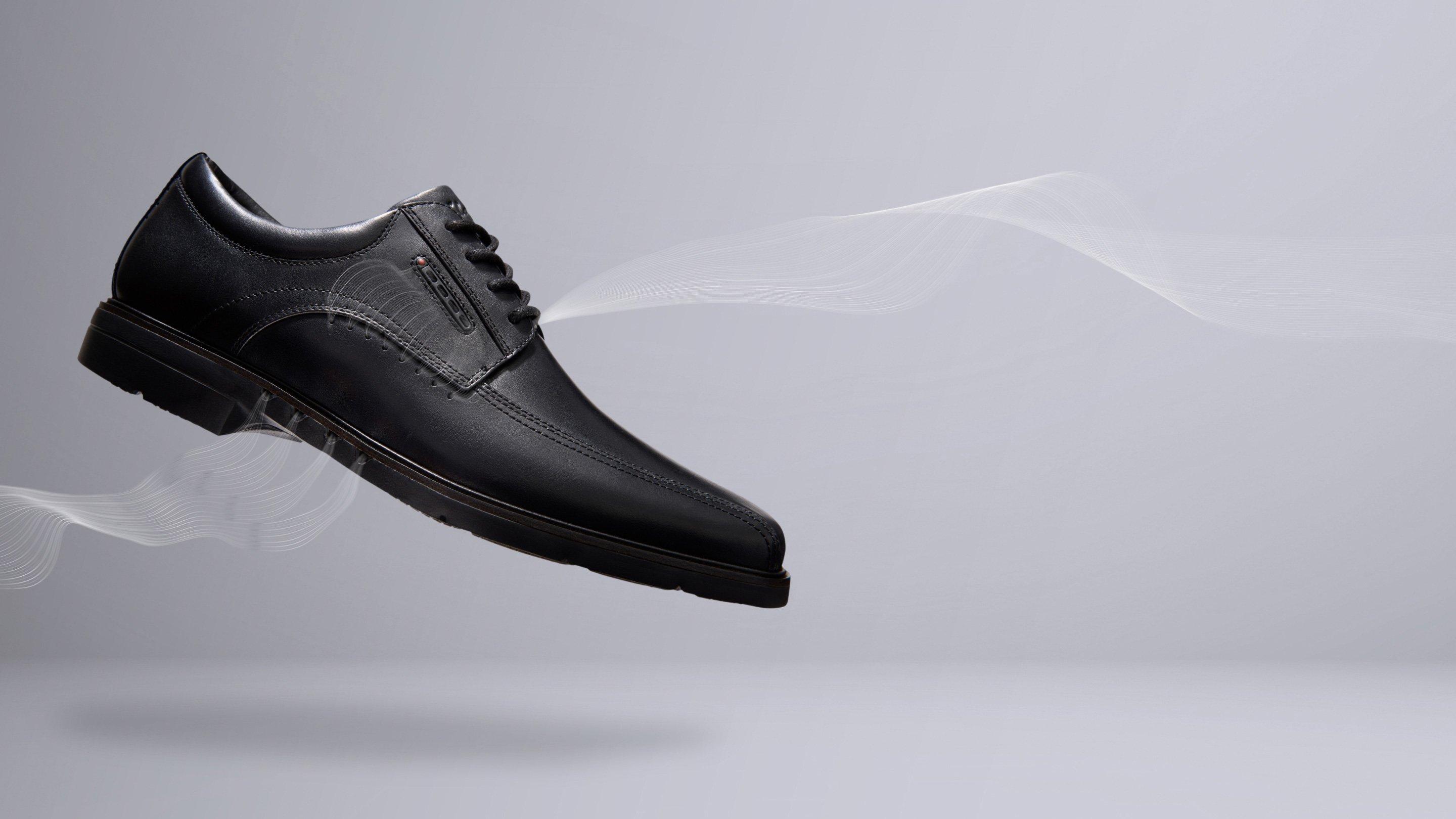 Clarks Unstructured smart black leather shoe Un Kendrick Way floats above ground with a graphic of air flowing through the shoe. The Clarks Unstructured logo appears to the right of the shoe. 