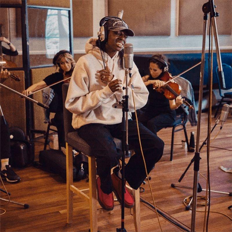 Cat Burns sitting on a high chair in a recording studio singing.