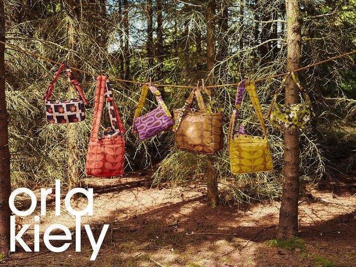 Colourful Orla Kiely patterned bags hanging between trees in woodland