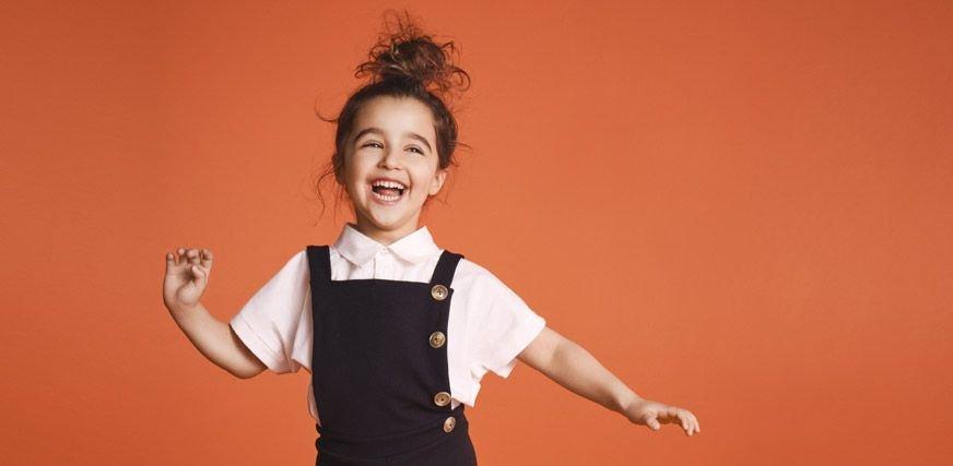 Laughing school girl wearing white school uniform shirt and black pinafore dress