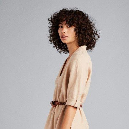 Above the waist shot of a woman wearing a stylish beige dress with a brown waist belt