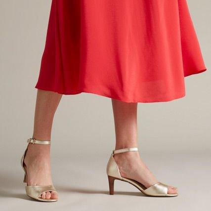 Below the knee shot of a woman wearing a metallic open toe wedding heel with a red skirt