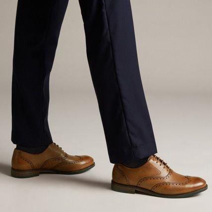 Below the knee shot of a man wearing brown leather brogue shoes with burnished detailing