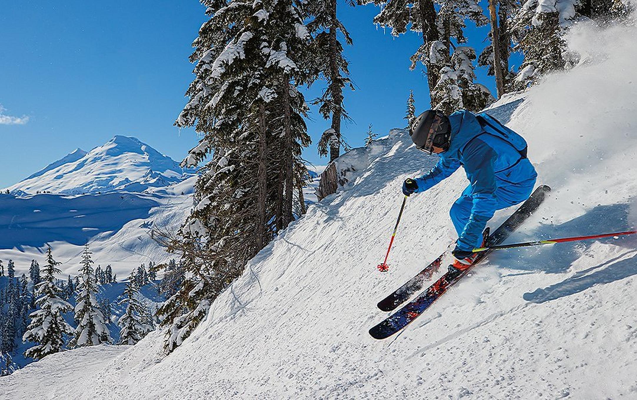 A skier wearing a blue jacket and pants skis down a powdery slope.