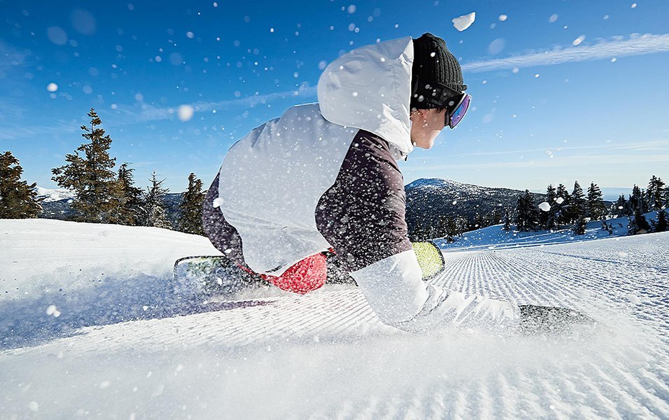 A snowboarder carves a deep turn on a freshly groomed ski run,