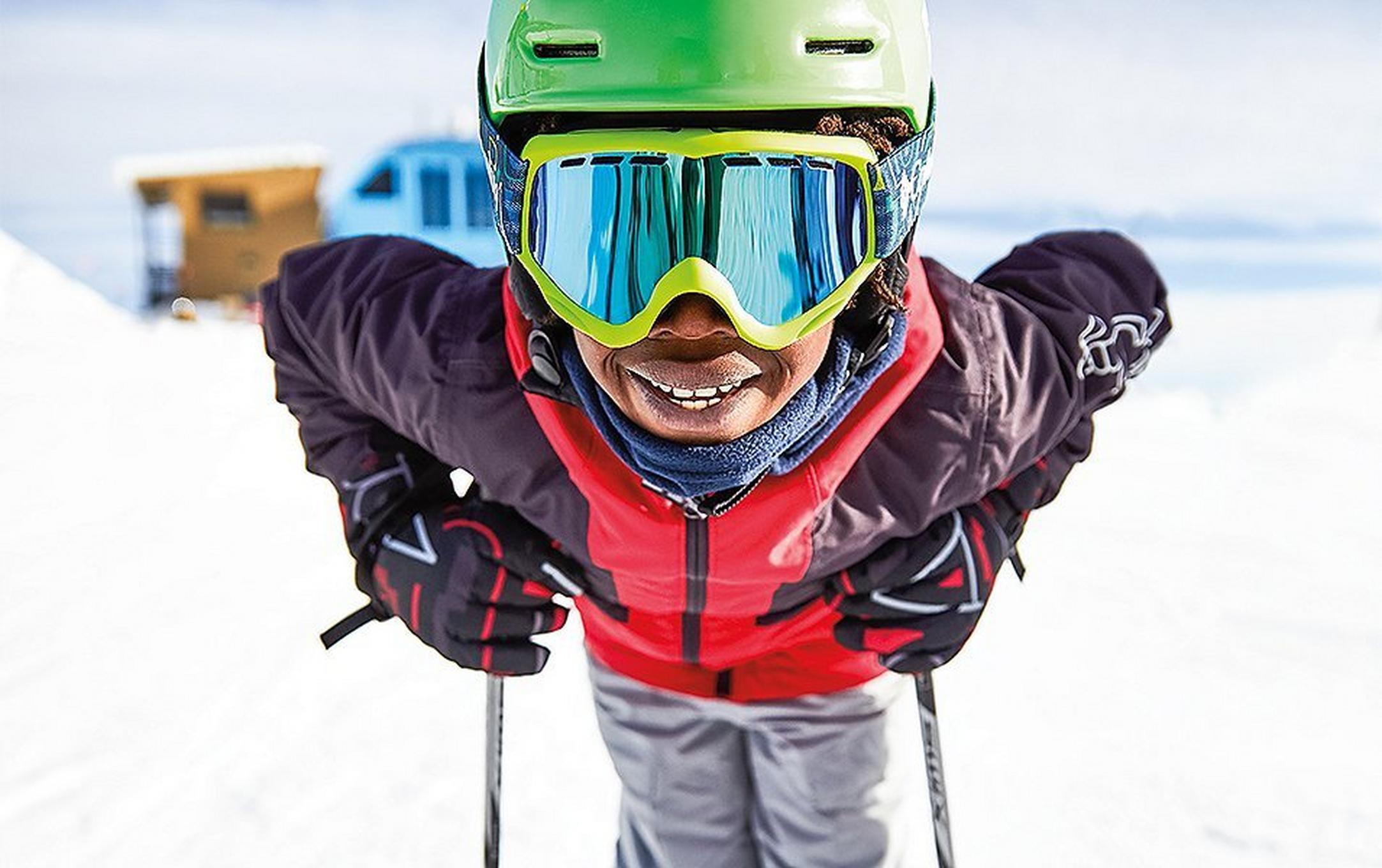 A young skier leans forward on his ski poles and smiles at the camera.