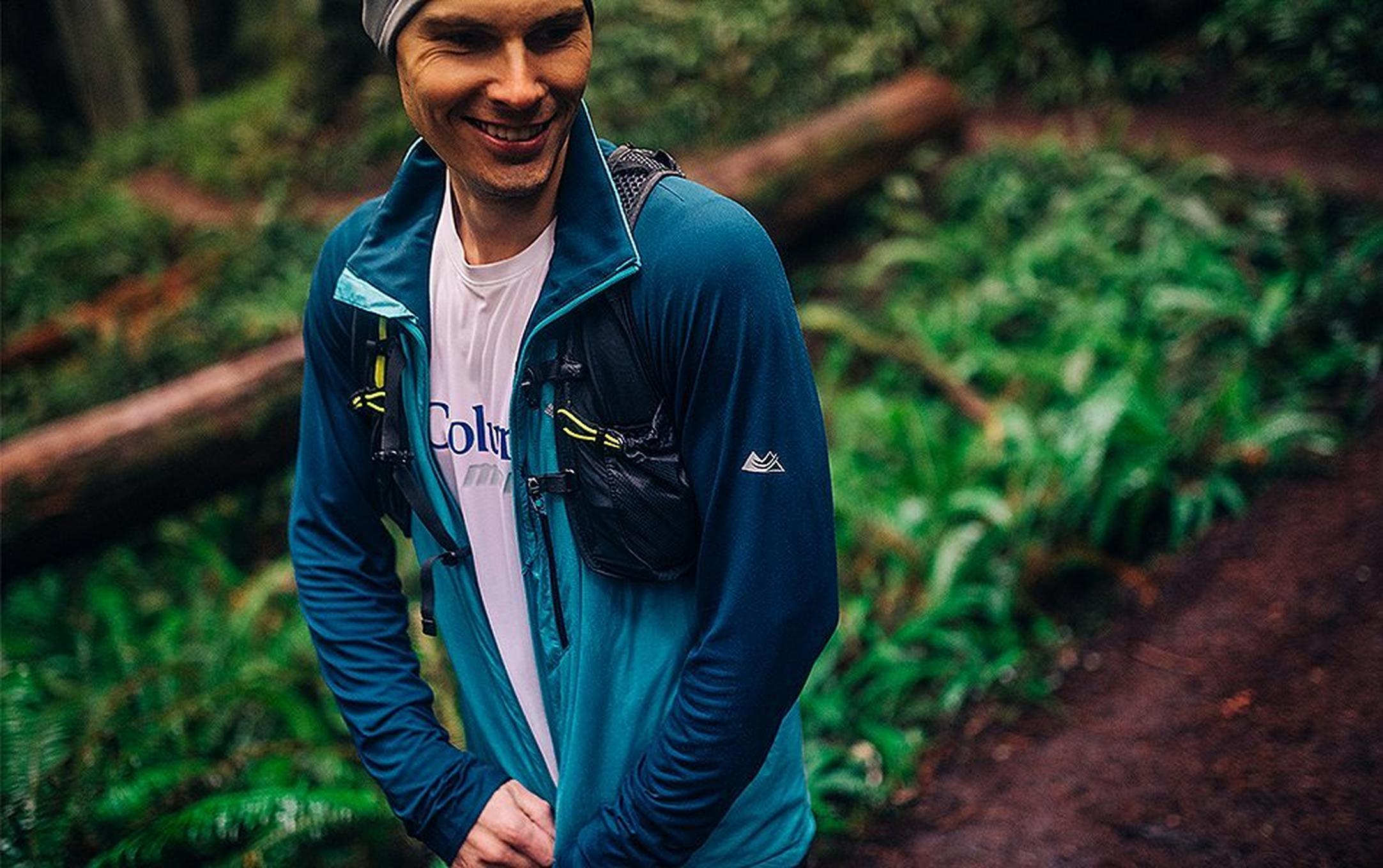 A man zipping up a coat in the woods.