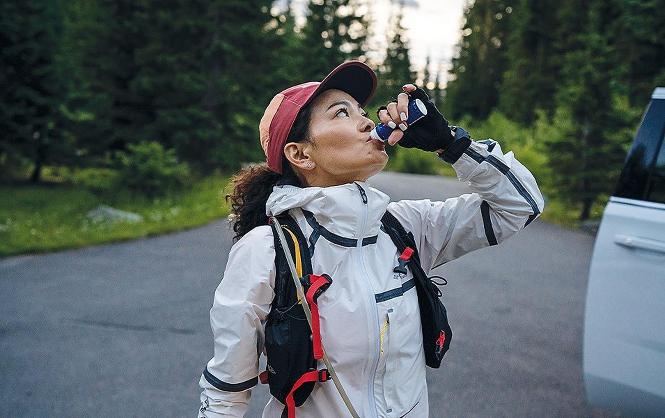 Woman in a parking lot drinking water.