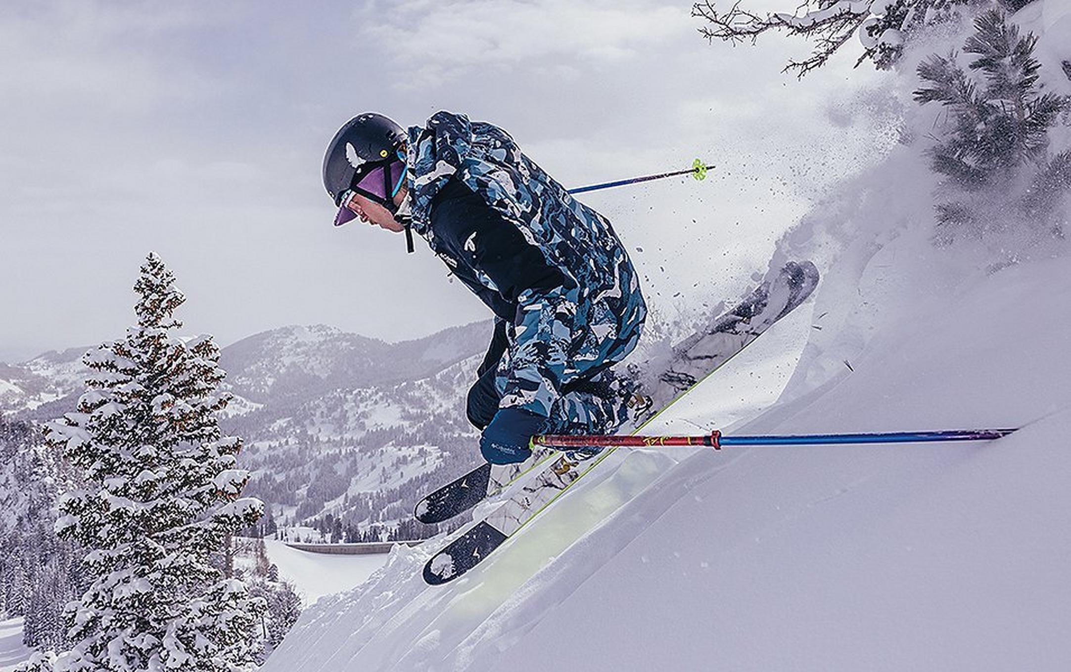 A skier catches air as he rips down a powder-filled ski run in a retro-style Columbia Sportswear ski suit.