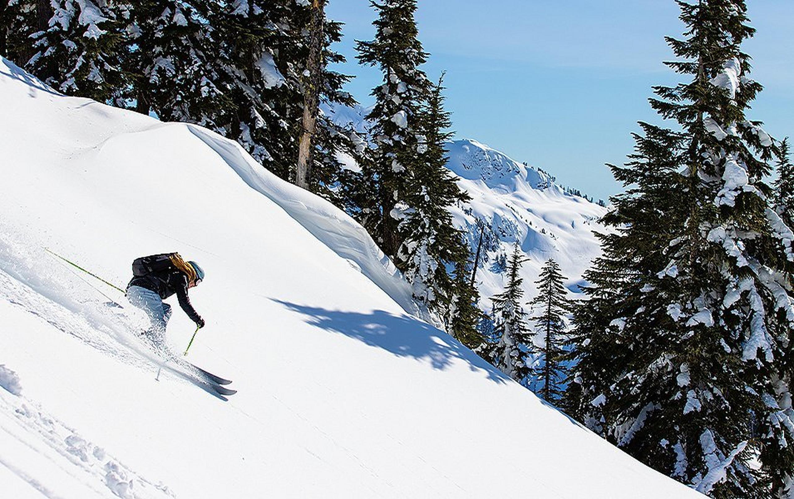 A skier rides down a mountain  slope in a fresh powder field on a sunny bluebird day.