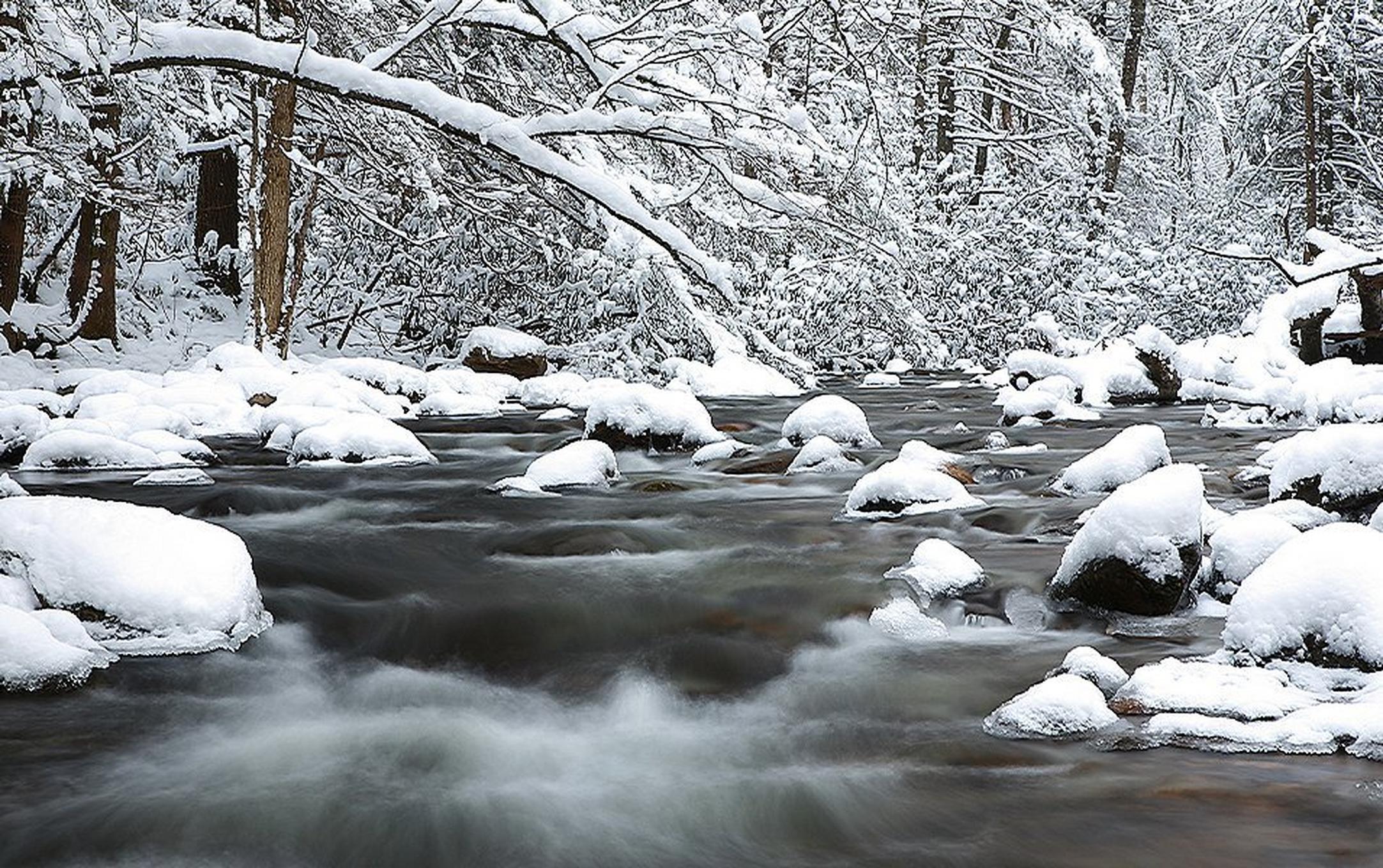 Snow-covered boulders line a flowing river as it rushes through a winter landscape in Great Smoky Mountains National Park.