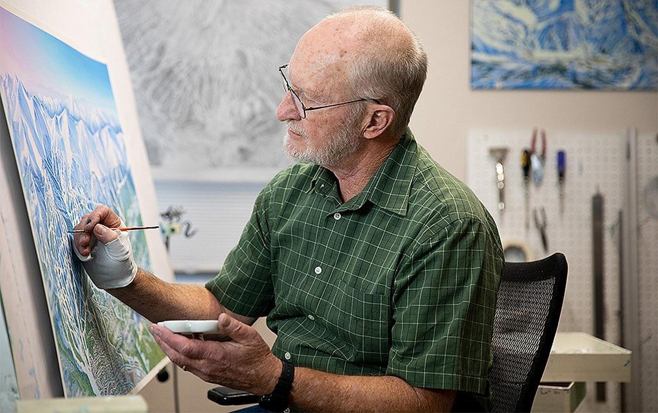 James Niehues sits at his easel holding a paintbrush and smiling for the camera.