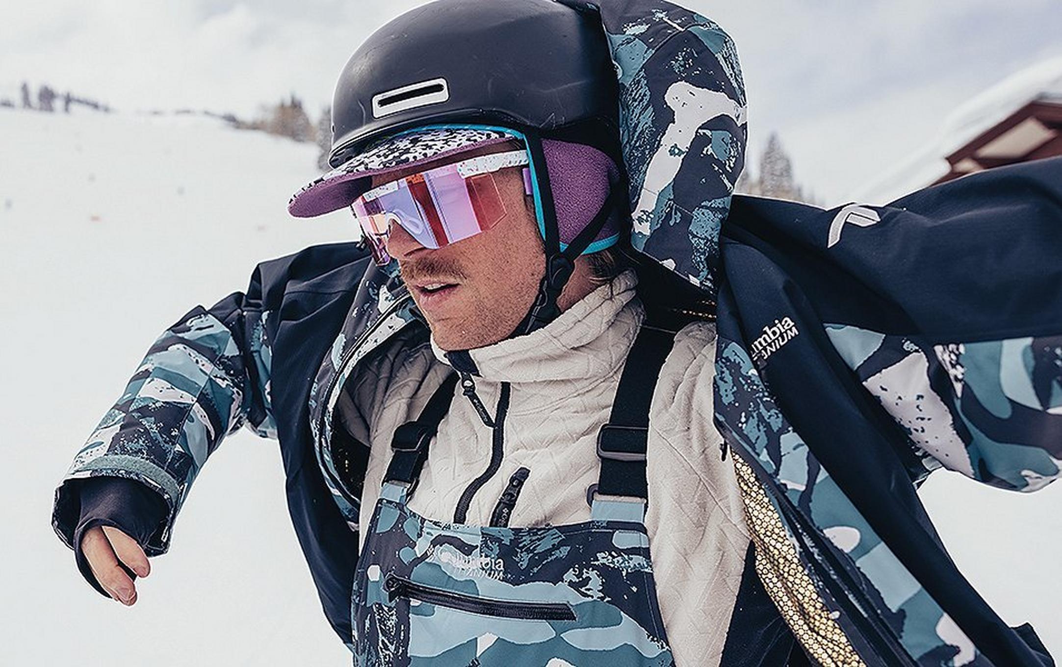 A skier takes off his blue Columbia Sportswear jacket, exposing his winter layers.