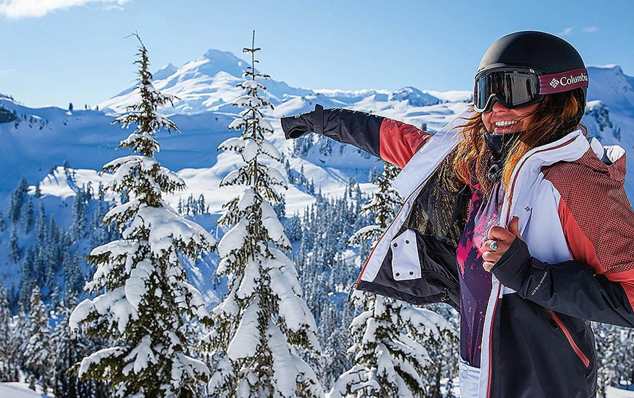 A skier takes off her jacket on a bright, sunny day on the mountain.