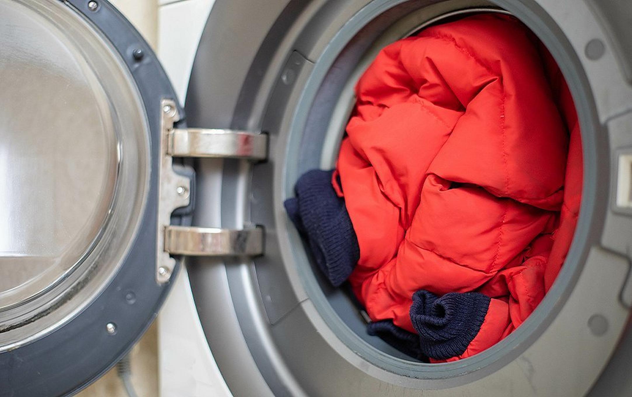 A  red puffer jacket sits in a washing machine with the door open.