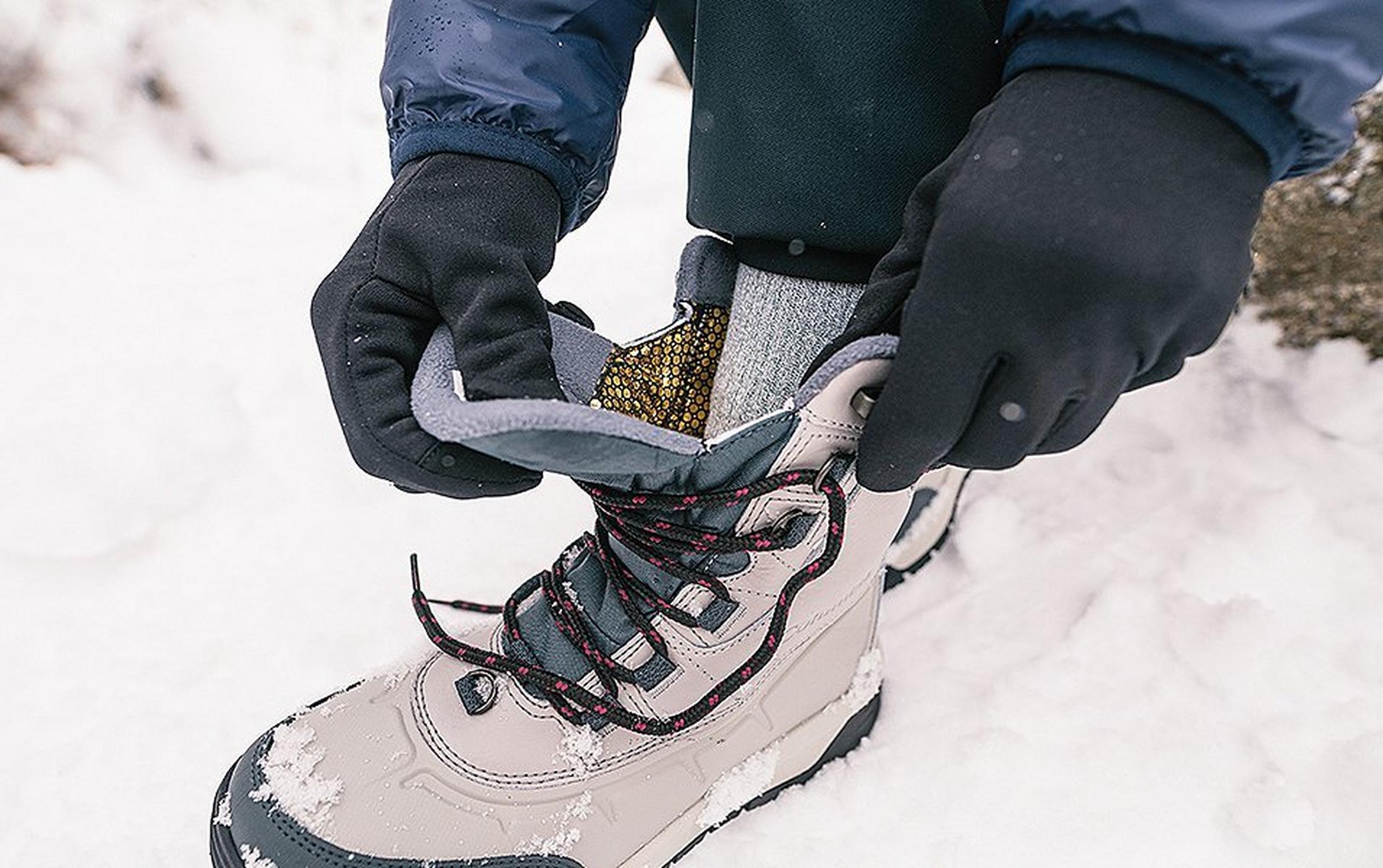 A winter camper ties his hiking boots in the snow.