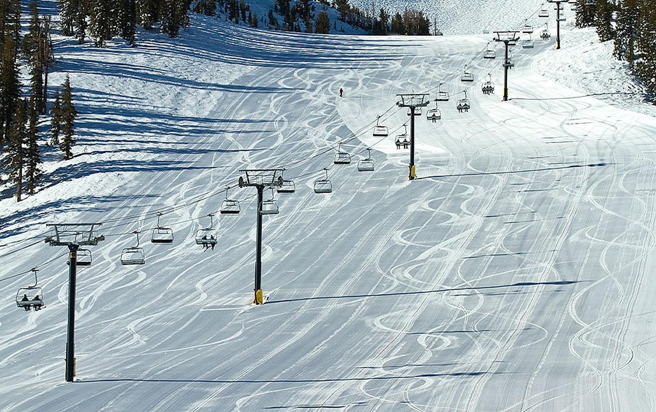 A wide landscape shot of a chairlift running up Mammoth Mountain on a sunny day.