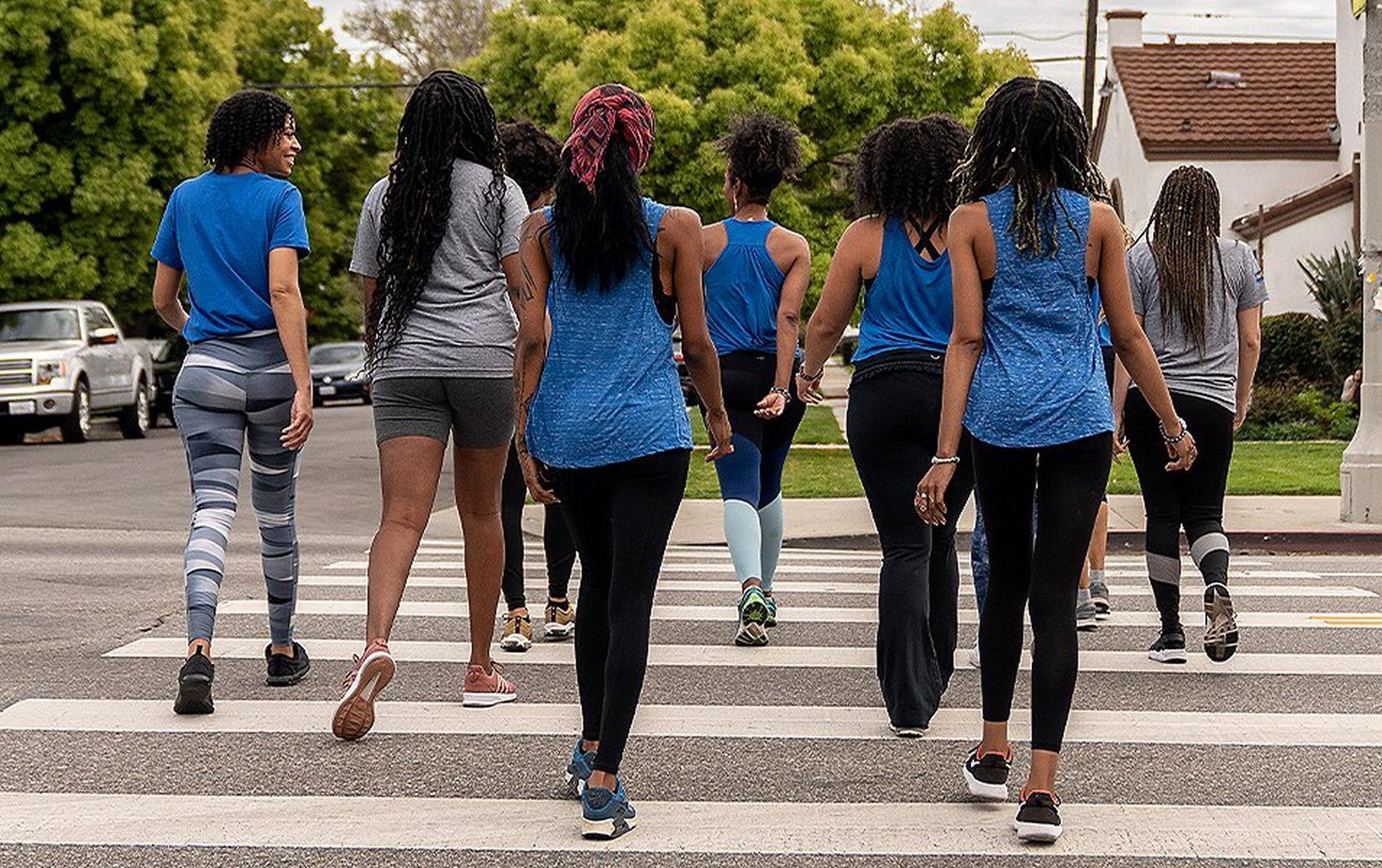 A photo showing the backs of six women in blue and white jackets walking across a street together.