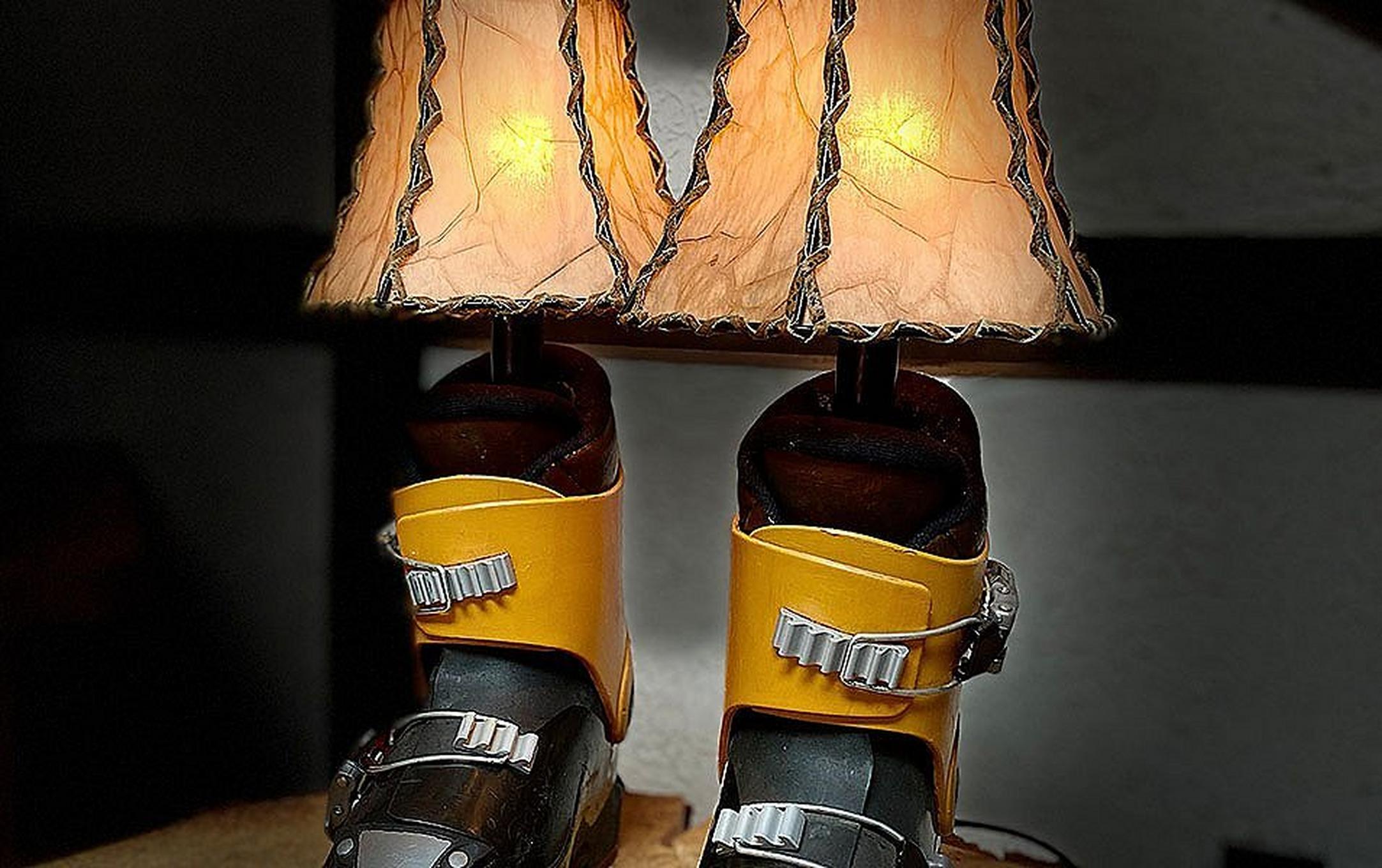 Two cute lamps made out of old ski boots sit on a small table in a dark room, emitting a soft glow.