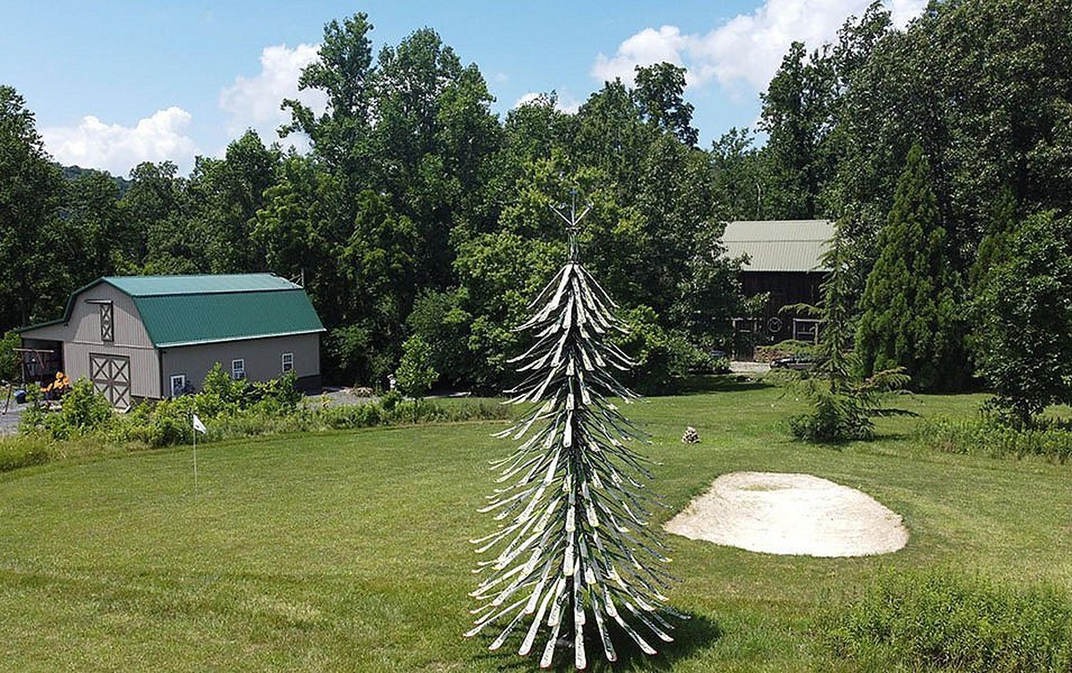 A tall tree made from skis stands on a beautiful piece of property featuring a scenic barn in the background.