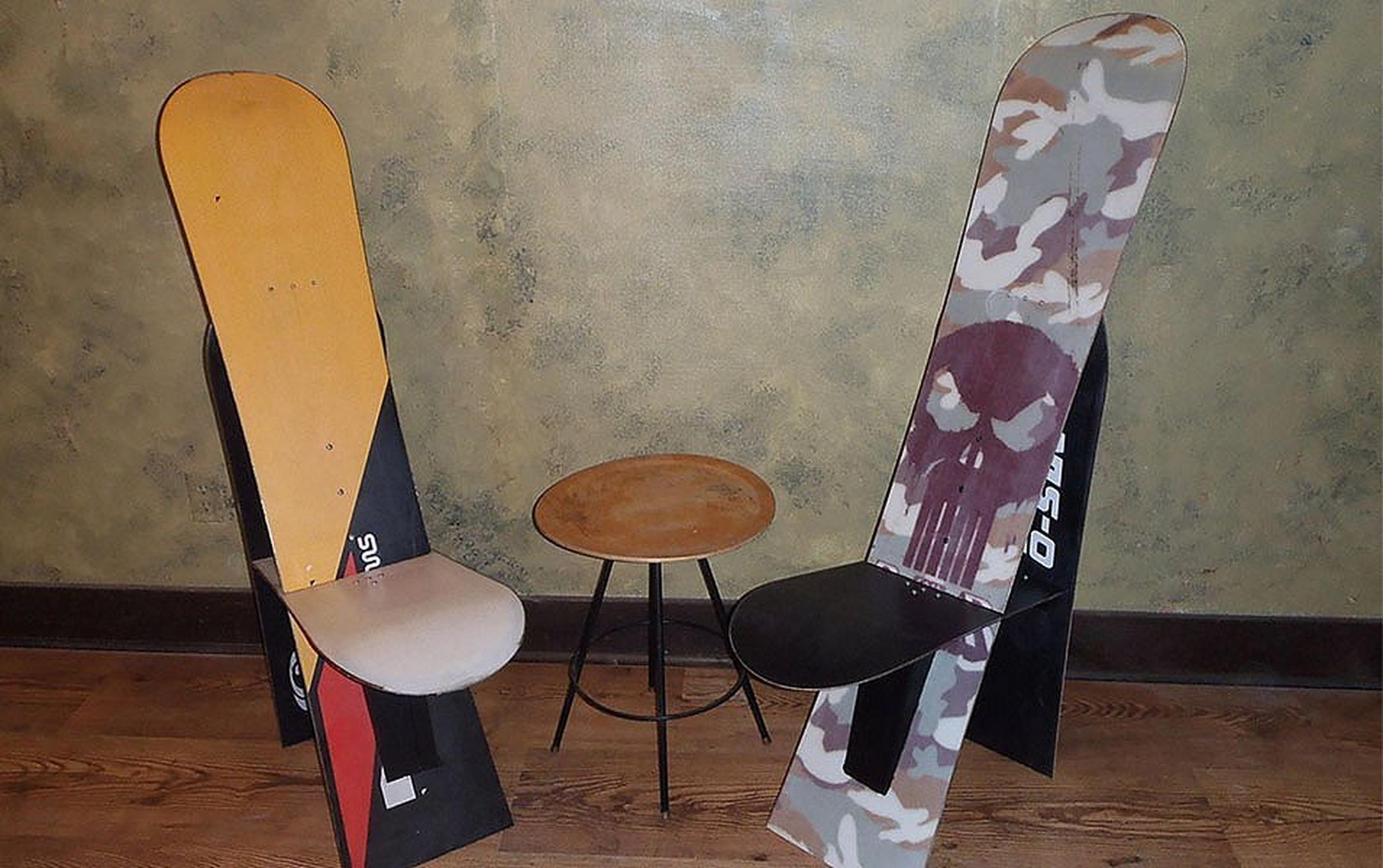 Two high-back seats made from recycled snowboards sit next to a small coffee table on a wood floor.